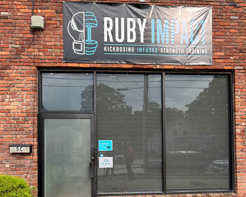 A brick building storefront with a large black banner reading 'RUBY IMPACT' and 'KICKBOXING INFUSED STRENGTH TRAINING' above dark window blinds.