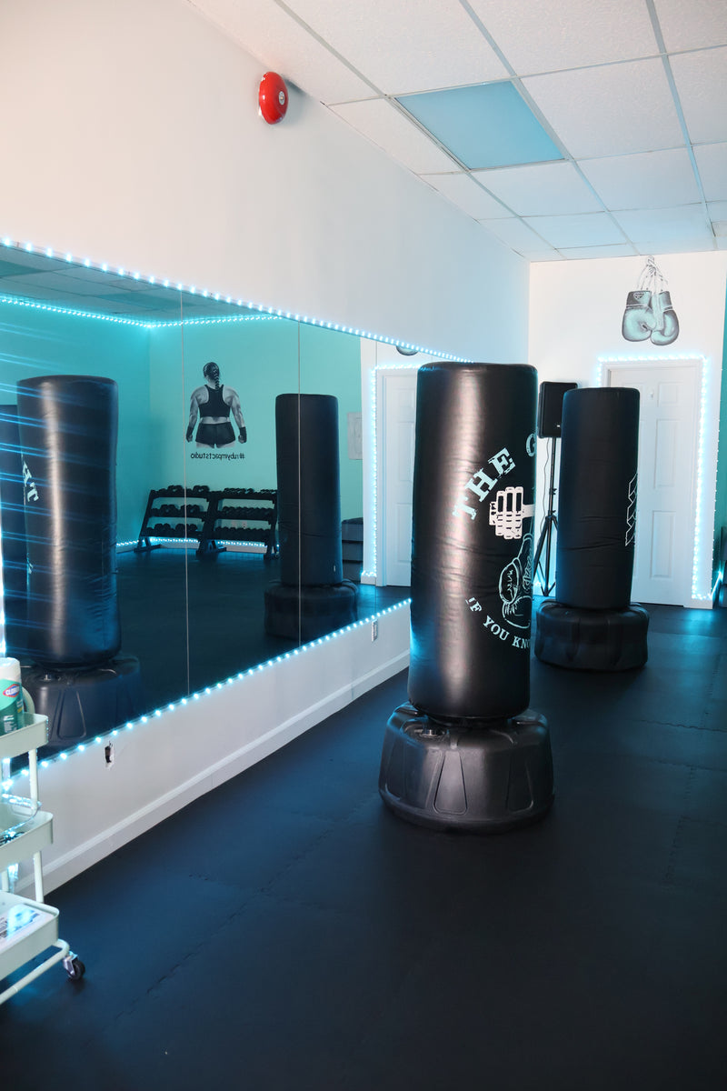 A black heavy punching bag with mirrored walls, blue LED lighting, and other punching bags in the background.